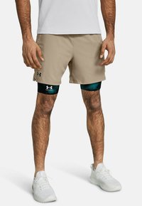 Beige Sportshorts aus leichtem Material mit einem elastischen Bund und dem Under Armour Logo. Darunter trägt die Person grüne Kompressionsshorts.