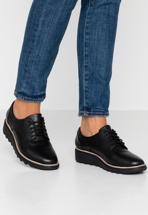 Zwarte leren veter schoenen met een afgeronde neus, voorzien van een dikke plateauzool en een lichtgekleurde accent langs de rand.