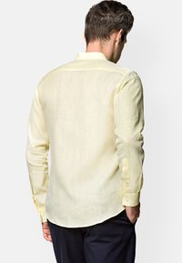 Jasnożółta, długosleeve koszula wykonana z teksturowanej tkaniny, z kołnierzykiem na guziki i zapinanymi mankietami, z zaokrąglonym dołem.