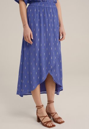 Zwiewna fioletowa spódnica midi z metalicznymi złotymi akcentami, wyposażona w elastyczny pas i boczny rozporek, zestawiona z brązowymi, paskami ozdobionymi sandałami na wysokim obcasie.