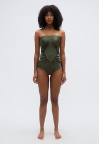 Μαγιό χωρίς τιράντες σε ελιά πράσινο με συγκεντρωμένο ύφασμα και διαμαντένια λεπτομέρεια μπροστά, κατασκευασμένο από λείο, ελαστικό υλικό.