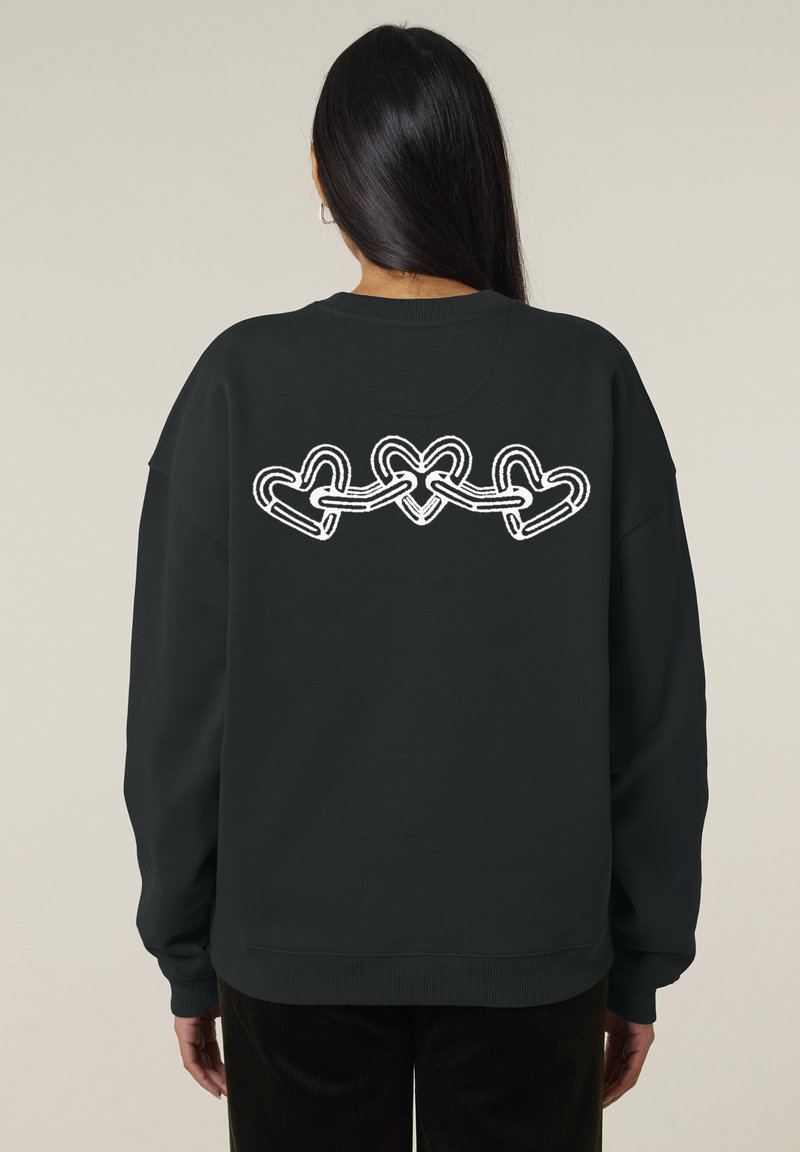 Sweatshirt noir à manches longues, avec un graphique blanc de cœurs entrelacés dans le dos. Poignets et ourlet côtelés.