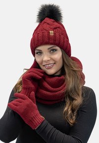 Cappello di lana rossa con pompon in pelliccia nera, sciarpa e guanti coordinati. Motivo testurizzato con accenti a coste. Tessuto spesso e caldo.