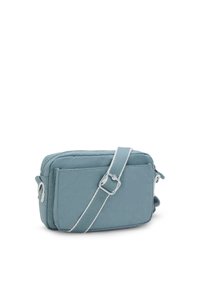 Blue fabric crossbody bag with a zip closure, adjustable strap, and a small pom-pom detail. Features a rectangular shape and soft texture.