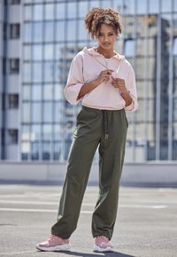 Lichtroze cropped hoodie met een rits aan de zijkant, gecombineerd met olijfgroene joggers met een elastische tailleband en lichtroze sportschoenen.