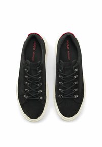 Mustat lenkkarit, joissa on mokkanahasta ja kankaasta valmistettu yläosa, kontrastiväriset punaiset yksityiskohdat kantapäällä sekä hopeiset silmukat ja tummat nauhat.