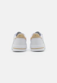 Białe trampki z chropowatą cholewką ze skóry zamszowej i skóry licowej. Kwadratowy obcas, złote akcenty na tyle oraz gruba biała gumowa podeszwa.