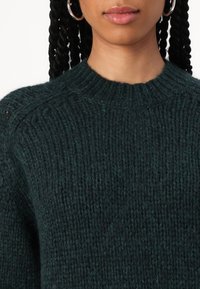 Grober dunkelgrüner Strickpullover mit Rundhalsausschnitt und strukturiertem Stoff. Verfügt über enge Rippungen am Hals und an den Schultern.