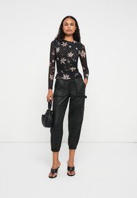 Top negro de manga larga con estampado floral, combinado con pantalones cargo de cuero negros y sandalias negras de tacón, sosteniendo un pequeño bolso negro.