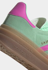 Baskets en suede vert avec des accents en cuir rose, langue en textile menthe texturée et semelle en gomme transparente. "Gazelle" en doré sur le côté.