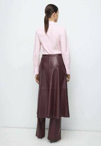 Fustă lungă din piele burgundă, asortată cu o cămașă roz deschis cu nasturi, având un contur structurat și o textură netedă.