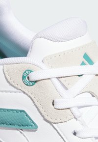 Weißer Sneaker mit samtigen Akzenten in Beige und Türkis, ausgestattet mit einem strukturierten türkisfarbenen Logo, flachen weißen Schnürsenkeln und einer Netz-Zunge.