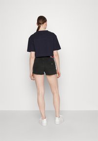 Camiseta navy recortada combinada con pantalones cortos de mezclilla negra con dobladillos deshilachados, vista desde atrás, complementada con zapatillas blancas.