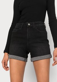 Svarta shorts i denim med hög midja, uppvikta fållar och kontrasterande grått innerfoder. Har framfickor och knapplåsning.