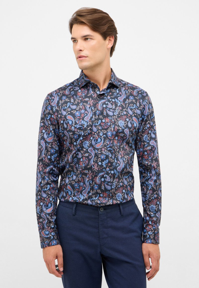 Lange mouwen shirt met een donker marineblauwe achtergrond en ingewikkelde bloemen- en paisleypatronen in blauwe, rode en roze tinten. Met knoopsluiting bij de kraag.