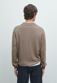 Maglione marrone a maglia con colletto, vestibilità rilassata e maniche lunghe. Materiale texturizzato con leggere variazioni di tonalità. Pantaloni scuri con cintura.