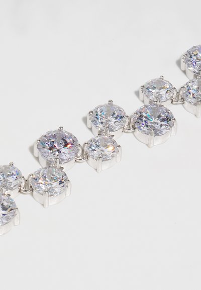 Ασημένιο μεταλλικό βραχιόλι με στρογγυλους, διαφανείς κρύσταλλους με επίπεδες επιφάνειες, συνδεδεμένο με κυκλικά στηρίγματα. Έχει λεία υφή, γυαλιστερό φινίρισμα και ρυθμικό σχέδιο.