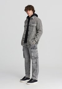 Szary dżinsowy kurtka na czarnej bluzie z kapturem, w połączeniu z dopasowanymi szarymi spodniami cargo. Posiada kieszenie oraz teksturowany materiał. Czarne sneakersy dopełniają stylizację.