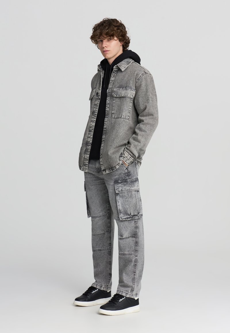 Szary dżinsowy kurtka na czarnej bluzie z kapturem, w połączeniu z dopasowanymi szarymi spodniami cargo. Posiada kieszenie oraz teksturowany materiał. Czarne sneakersy dopełniają stylizację.