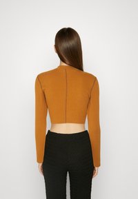 Kortärmad långärmad topp i orange ribbat tyg med hög hals. Har kontrasterande sömmar och en figursydd design, parat med svarta texturerade byxor.