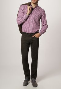 Rood-wit geblokte overhemden, een bruin suede jack over de schouder, donker olijfgroene broek en grijze schoenen met blauwe accenten.