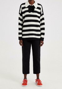 Sort og hvid stribet sweater med en hvid krave og flæset lukning, kombineret med sorte bukser og røde sneakers. Minimalistisk design.