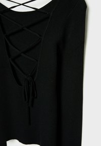 Haut noir en tricot côtelé à manches longues avec un décolleté en V profond et un détail de laçage croisé noué en un nœud à l'avant.