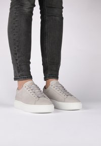 Sneakers in suede grigio chiaro con suola in gomma bianca, caratterizzati da una punta rotonda, lacci anteriori e un branding discreto sulla linguetta.