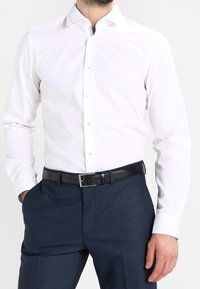 Biała koszula z długimi rękawami, kołnierzykiem na guziki i niebieskim detalem akcentowym. Połączona z granatowymi teksturowanymi spodniami i czarnym paskiem.