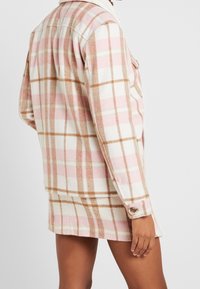 Flanell skjortejakke i rosa og kremfarget rutete med brune detaljer, med krage og knappede mansjetter, laget av myk teksturert stoff.