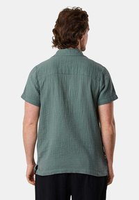 Camicia a maniche corte in tessuto verde strutturato, con colletto, vestibilità rilassata e spacchi laterali nell'orlo, vista da dietro.