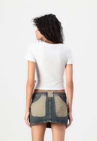 T-shirt bianco a maniche corte e taglio cropped abbinato a una gonna di jeans con tessuto bicolore, tasche frontali e dettagli di cucitura a vista.