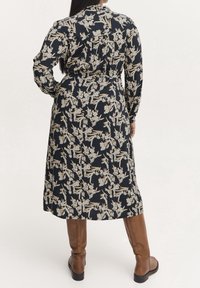 Mönstrad klänning i mörkblått med långa ärmar, krage med knappar och åtdragen midja. Bärs med bruna knähöga stövlar.