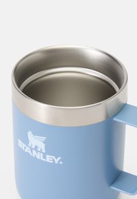 Ceramiczny kubek o matowej jasnoniebieskiej powierzchni, ze stali nierdzewnej na krawędzi oraz bocznym uchwytem. Na kubku znajduje się logo "STANLEY" w kolorze białym.