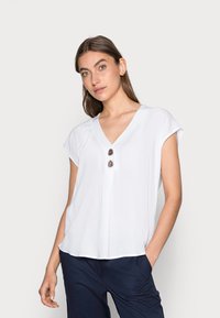 Witte blouse met korte mouwen en een V-hals, met twee ronde bruin knopen aan de voorkant en een losse, vloeiende ontwerp voor comfort.