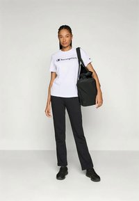 Hvid bomulds-T-shirt med "Champion"-logo, parret med sorte slim-fit bukser og sorte sneakers; holder en sort tote-bag.
