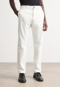 Hvite, rette bukser med knappelukking, laget av et glatt materiale, med sidelommer og et rent, minimalistisk design. Sorte sko.