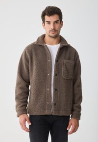 Jachetă din fleece maronie cu guler, nasturi frontali și un buzunar pe pieptul stâng. Material texturat și design relaxat.