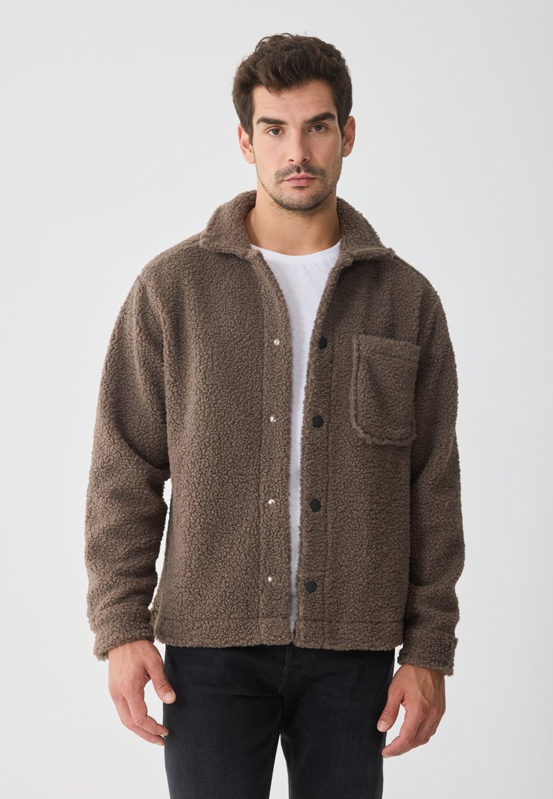 Bruine fleecejas met een kraag, knopen aan de voorkant en een zak op de linkerborst. Getextureerde stof en een ontspannen pasvorm.