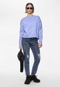 Light purple cropped sweatshirt, distressed blue jeans, black sneakers, and a small black shoulder bag, worn with dark sunglasses.