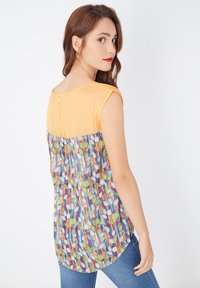 Blusa colorida que presenta una parte superior amarilla sólida con mangas de taza, que se transforma en una sección inferior multicolor con un patrón de formas de hojas abstractas.