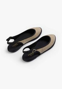 Pár béžových a černých slingback plochých bot s přezkami a texturovanými podrážkami, označených "Scalpers Made in Spain."
