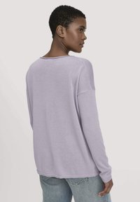 Lavendelfarbener, langärmeliger Strickoberteil mit lockerer Passform, weitem Ausschnitt und gerippten Bündchen, kombiniert mit hellen Jeans.