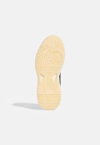 Svart sneakersula med texturerat gummi och cirkulära greppmönster, med varumärkeslogotyp i mitten och en beige yttersula för bra grepp.