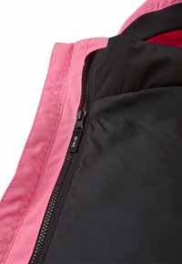 Interno di una giacca rosa e nera che mostra i dettagli della cerniera e la texture del tessuto, enfatizzando il contrasto dei colori e gli elementi di design.