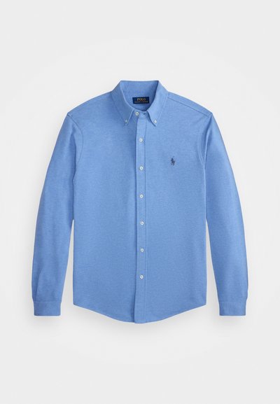 Világoskék, hosszú ujjú gombos ing, hegyes gallérral, melyen egy kis hímzett logó található a mellrészen, és sima pamut textúrával rendelkezik.