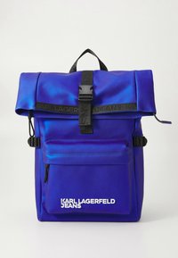 Kék matt hátizsák tekercselt felső záródással, fekete állítható pánttal, első cipzáras zsebbel és fehér "KARL LAGERFELD JEANS" logófelirattal.