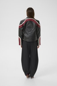 Woman wearing black leather jacket with red and white stripes and embossed rose design on the back, paired with wide black pants and maroon heels.