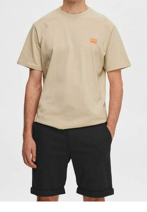 Beige bomuld t-shirt med et lille orange grafisk logo på venstre bryst, kombineret med sorte shorts med opkrogede ben.