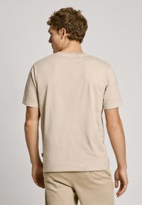 Camiseta de algodón beige con mangas cortas y cuello redondo, con una textura suave y un ajuste relajado, vista desde la parte trasera.